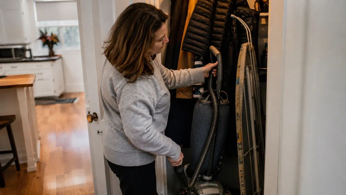 A heavy old upright vacuum wedged in a hall closet behind coats and an ironing board