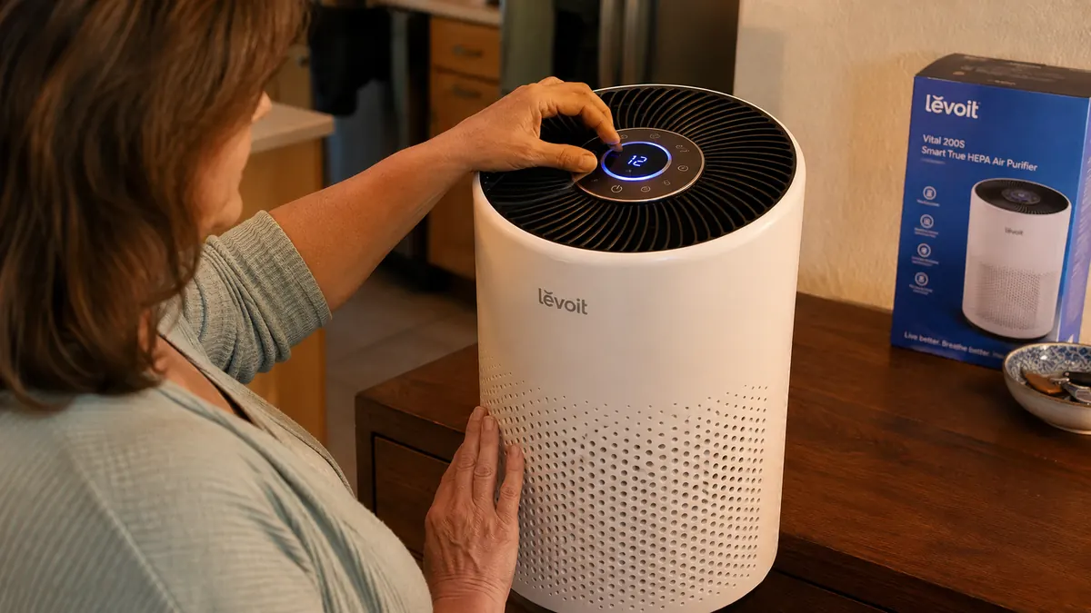 Hand adjusting the top control ring on the Levoit Vital 200S air purifier while it runs on a dresser